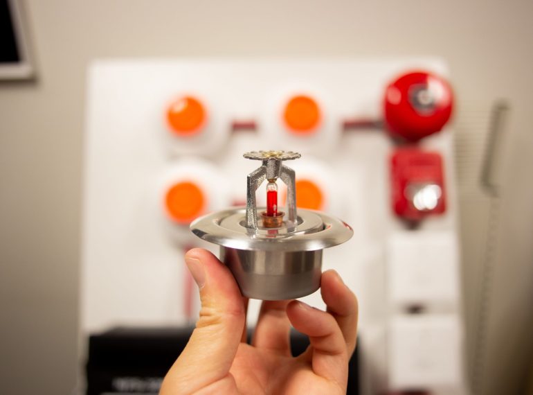 A hand holding a silver fire alarm system sensor